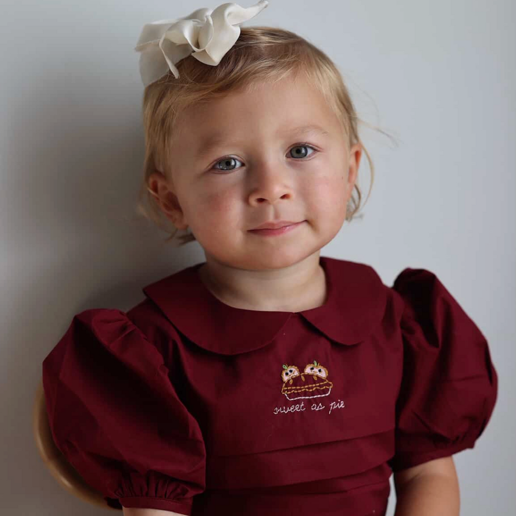 Young girl wearing a burgundy dress with a floral headband against a plain background